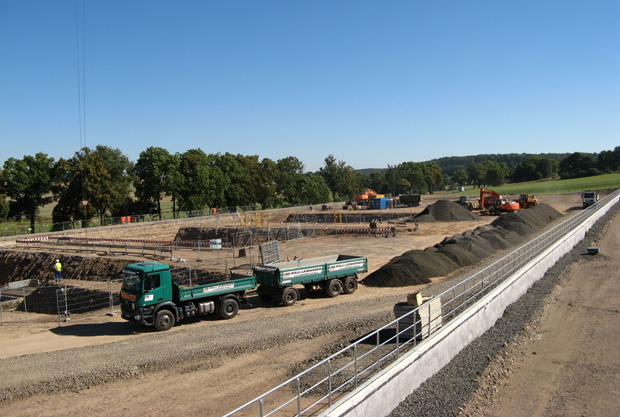 Blick auf die Baustelle: Man kann im Hintergrund bereits die drei Fundamente erkennen, auf denen bald die Verdichterhalle stehen wird. Jedes Fundament wird dann einen der von Gasturbinen angetriebenen Turbo-Verdichter tragen.